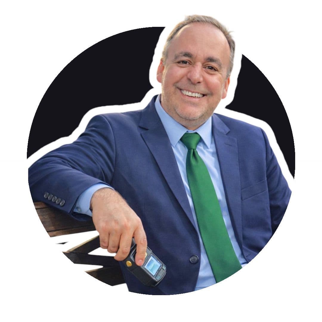 Homem sorridente de terno azul e gravata verde, segurando um pequeno dispositivo eletrônico.