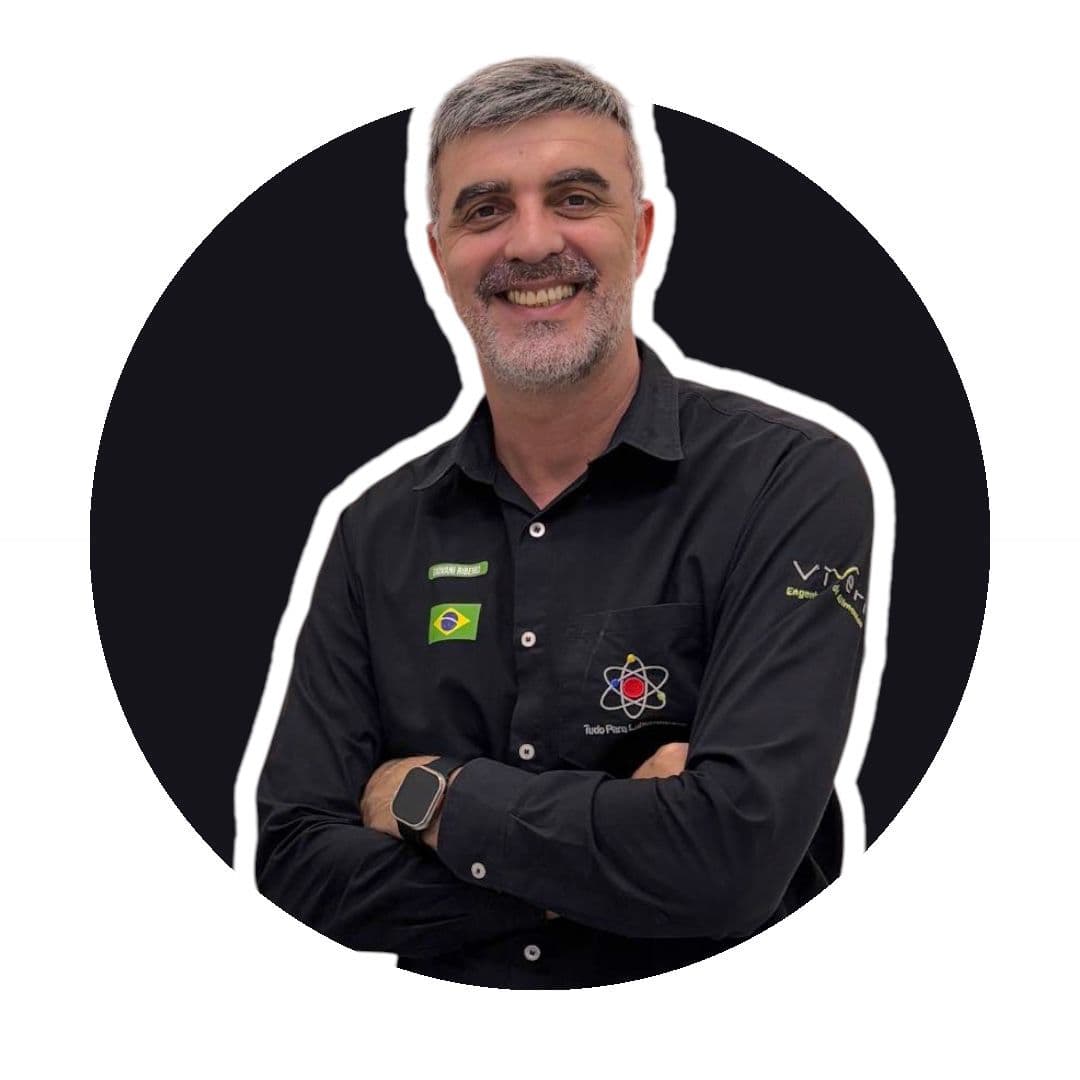 Homem sorridente de barba grisalha, braços cruzados, vestindo camisa preta com bandeira do Brasil.